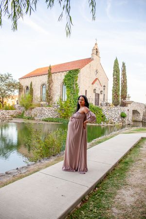 Elegant maternity photos taken outside stone church with cypress trees and water feature.