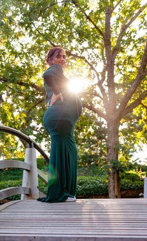 A silhouetted maternity pose on a wooden bridge during golden hour.