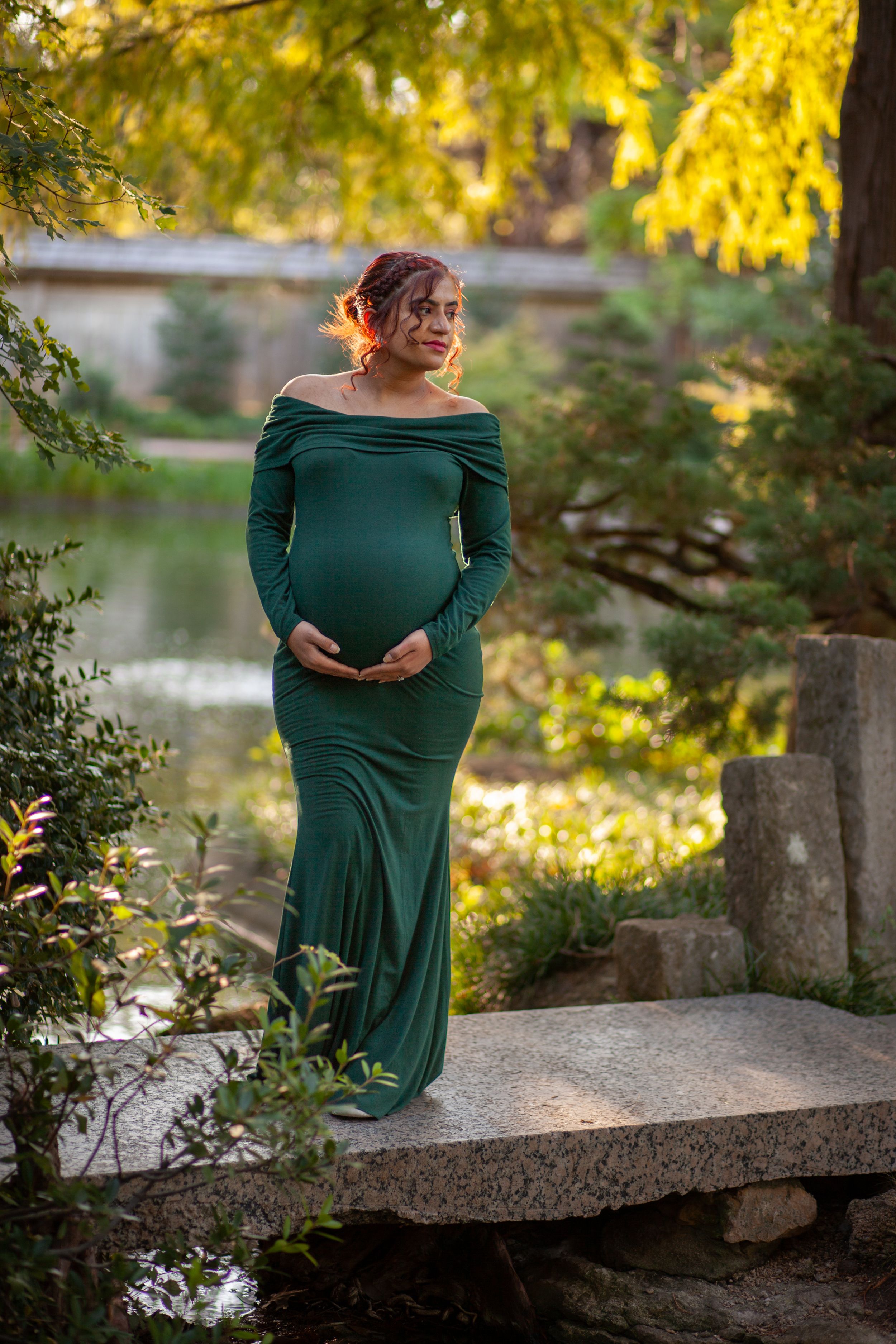 A maternity portrait in an emerald green dress amid autumn foliage.