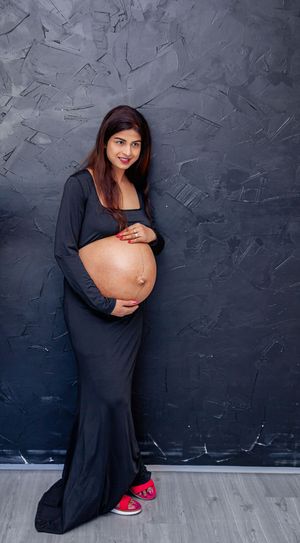 Maternity portrait against a textured grey wall featuring a long black dress.