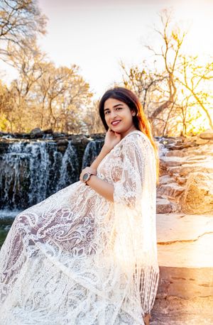 A maternity photo shoot by a waterfall with a person wearing a white lace dress.
