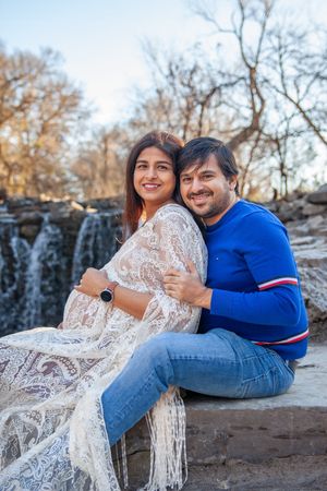 A couple sits together by a waterfall during an outdoor maternity photo session.