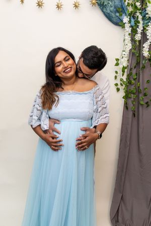Light blue maternity gown with lace details against white wall with hanging decorations.