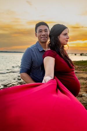 A couple embraces on a beach at sunset with a flowing red dress creating a romantic silhouette.