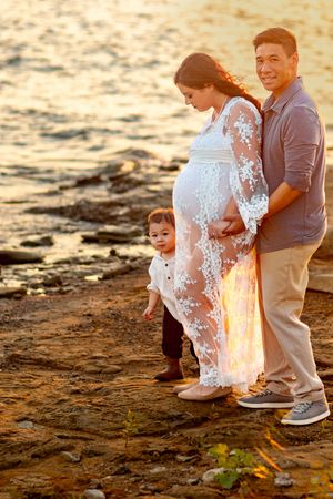 Family maternity photos on rocky beach shore during golden hour sunset.
