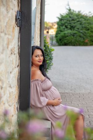 A person in a pink off-shoulder dress poses thoughtfully outdoors against a blurred background.