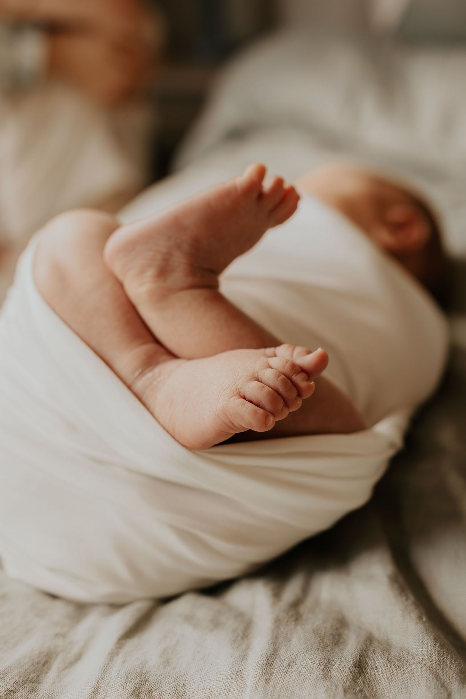 Close up of tiny baby feet wrapped in soft white blanket resting on grey bedding.