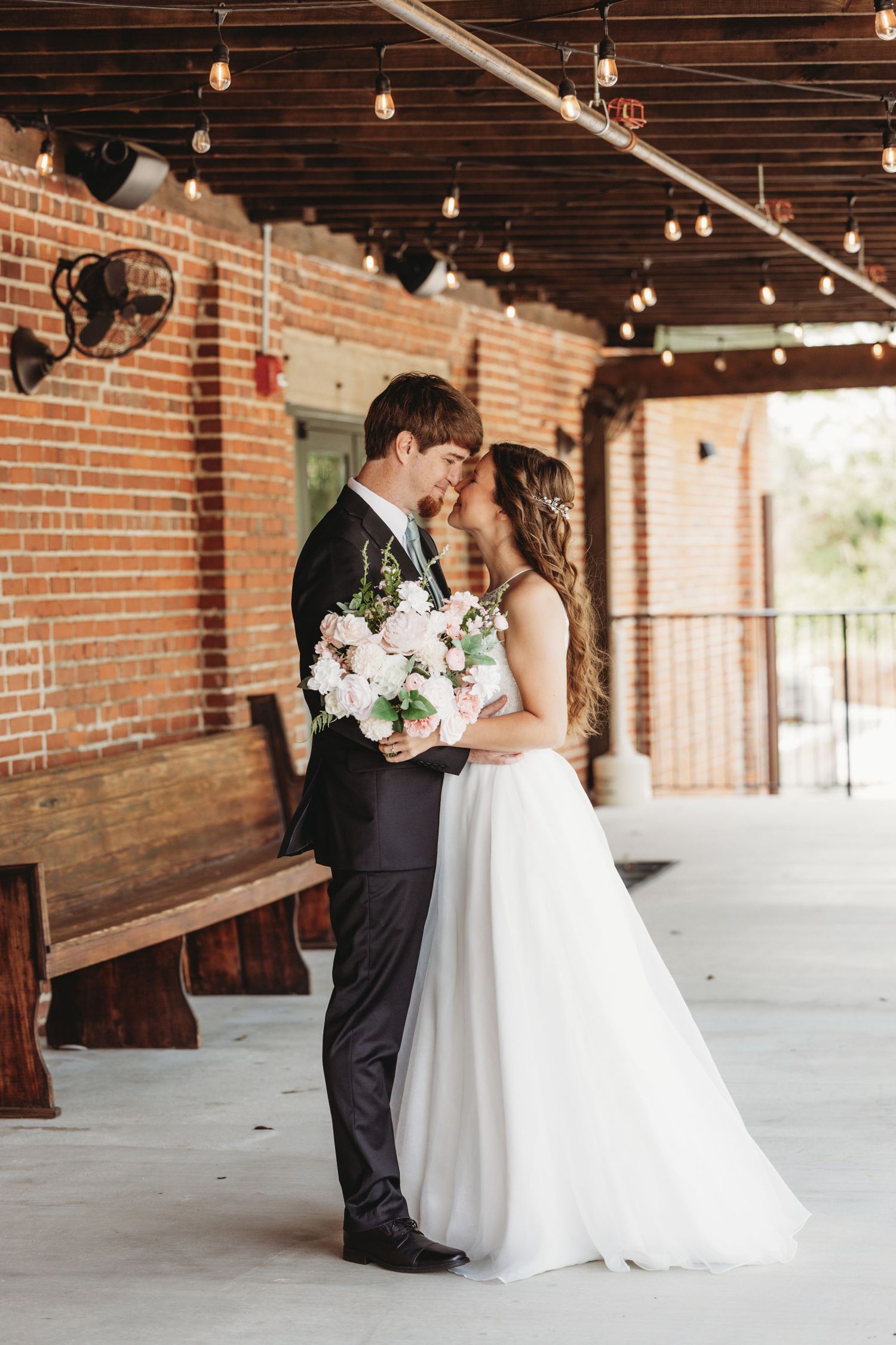Wedding couple sharing intimate moment under string lights in rustic brick venue.