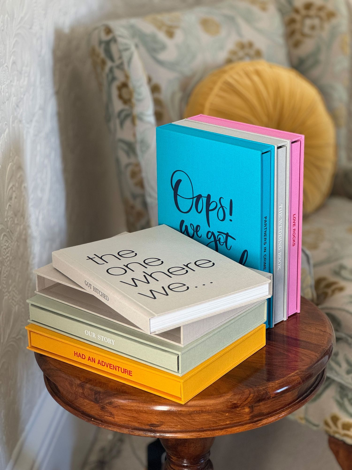 Multiple hardcover books with colorful spines are arranged on a round wooden side table.