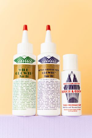 Three hair oil products sitting on a purple shelf with a tan backdrop.