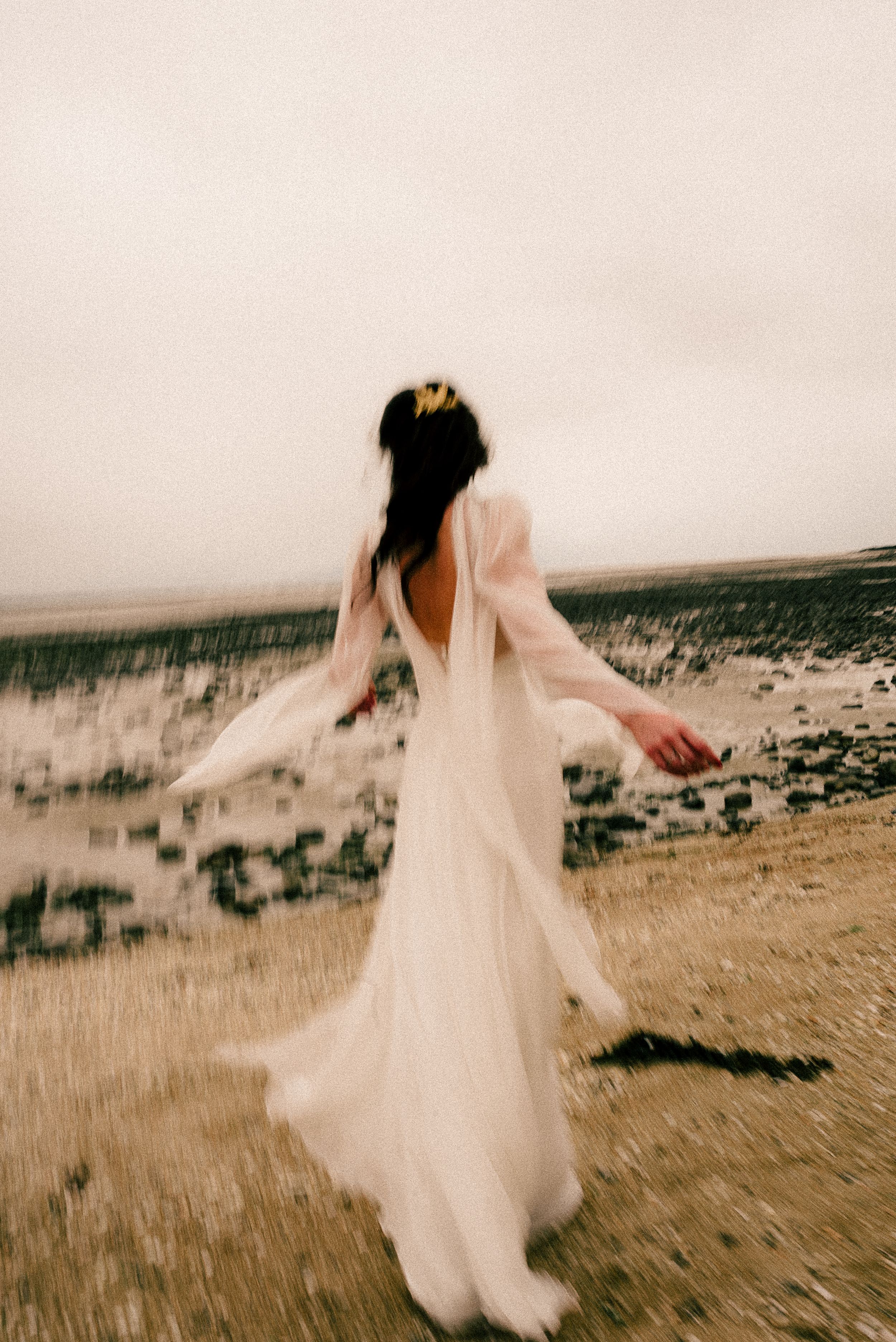 A bride in a flowing white wedding dress twirls and dances across a scenic coastal landscape in a series of motion photographs.