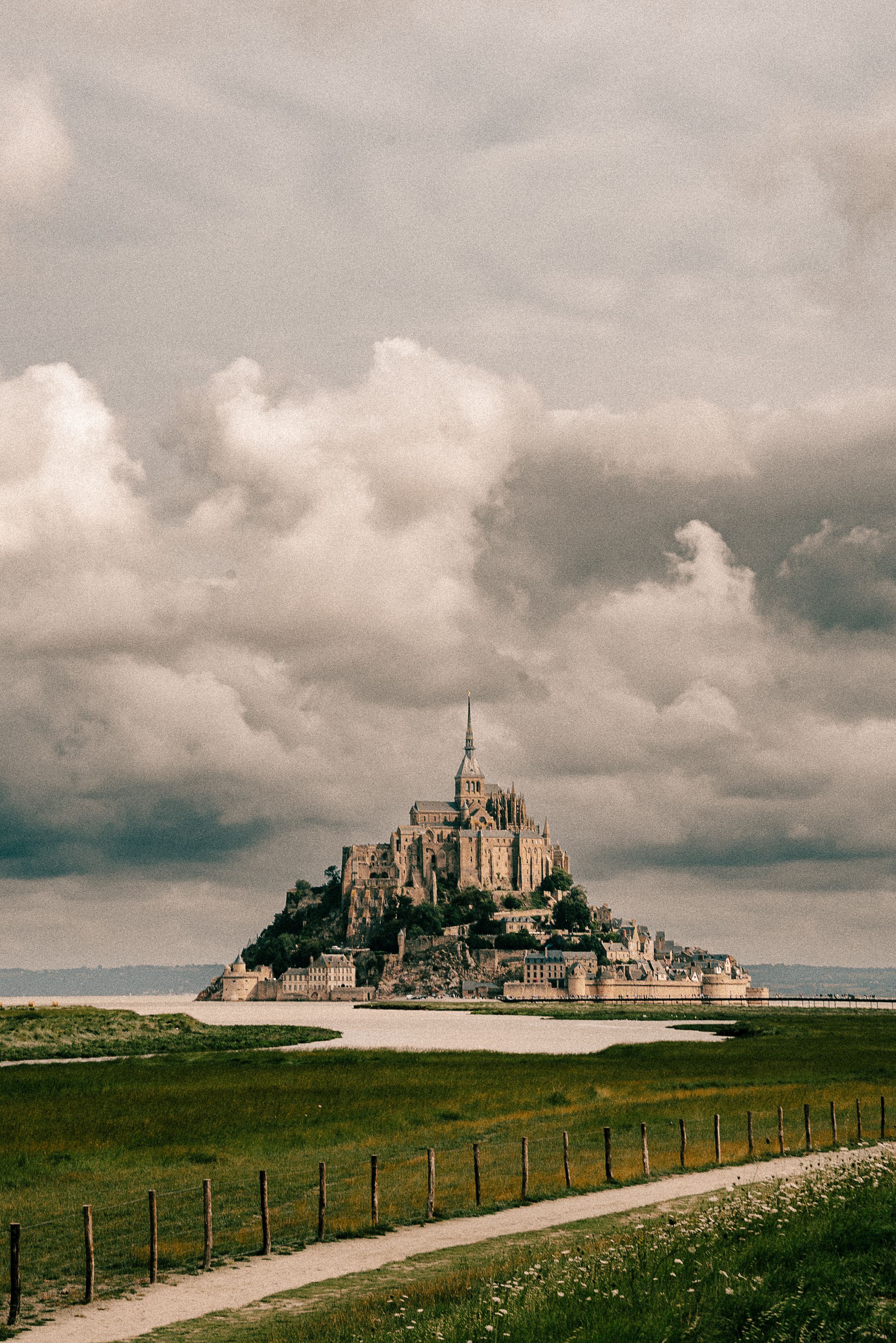 Mont Saint-Michel castle rises majestically from an island under dramatic cloudy skies in France.