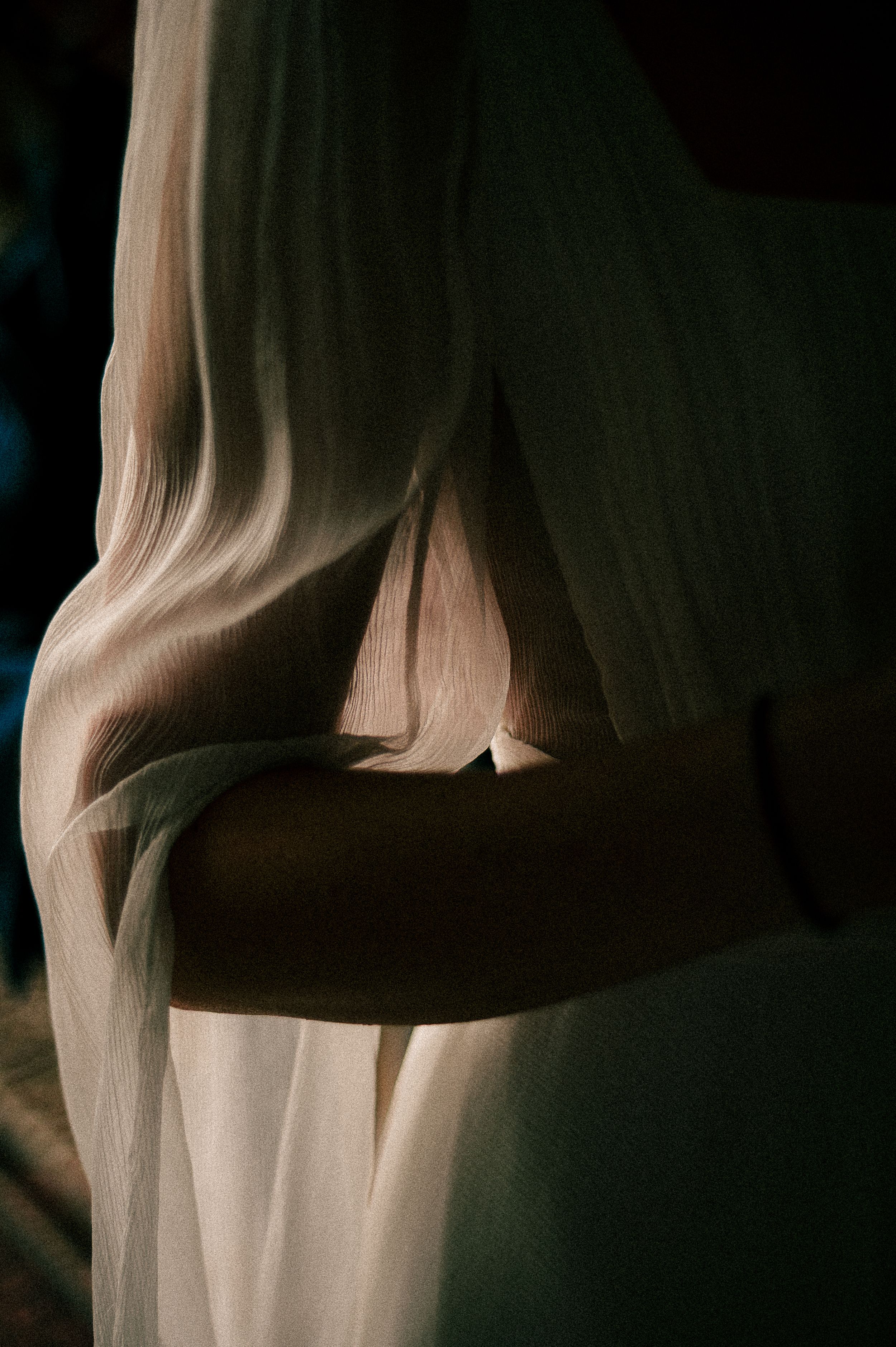 Artistic close-up of flowing white wedding dress fabric in dramatic lighting.