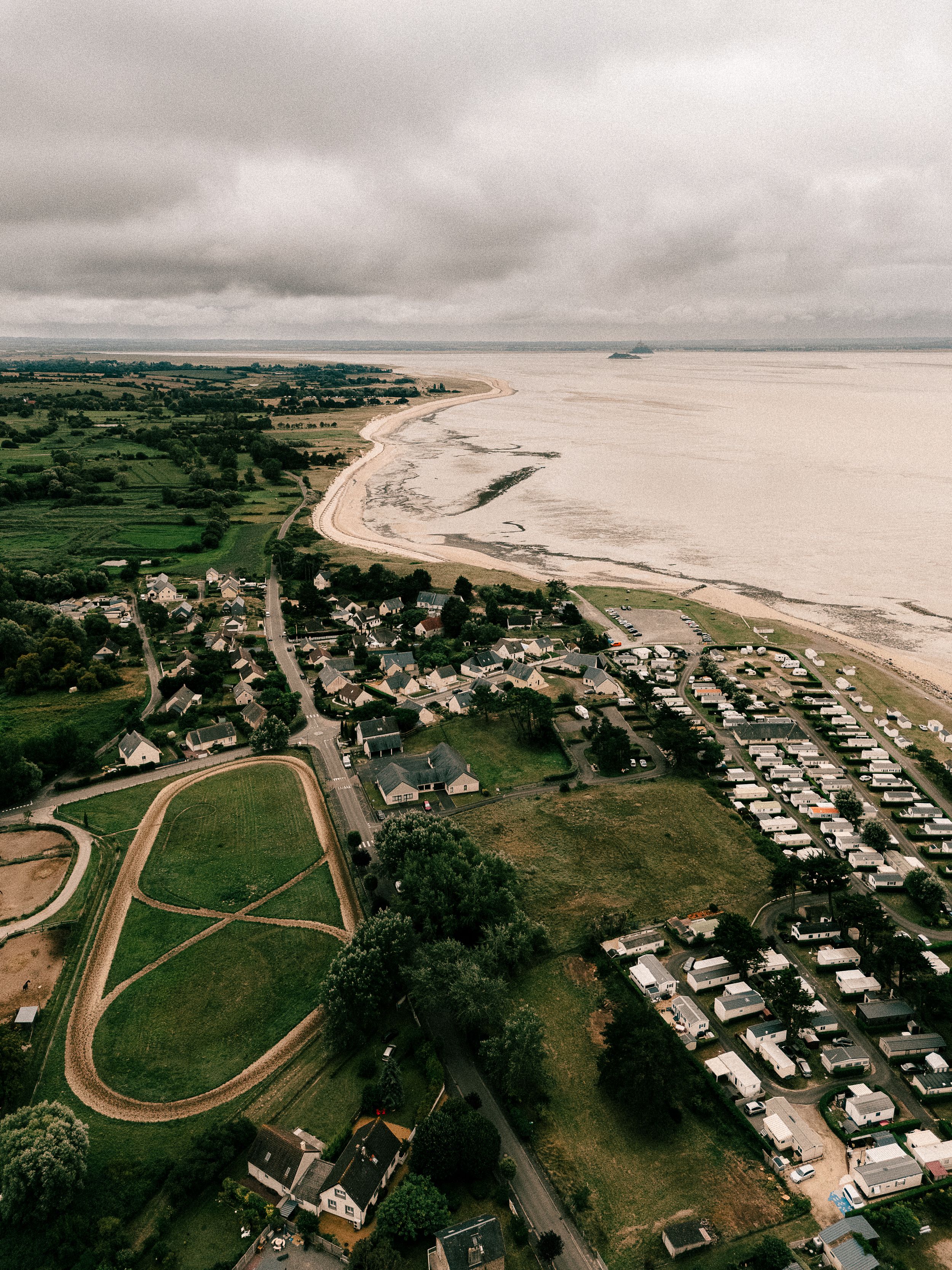 Aerial view of coastal town with beach, racetrack and residential areas under cloudy sky.