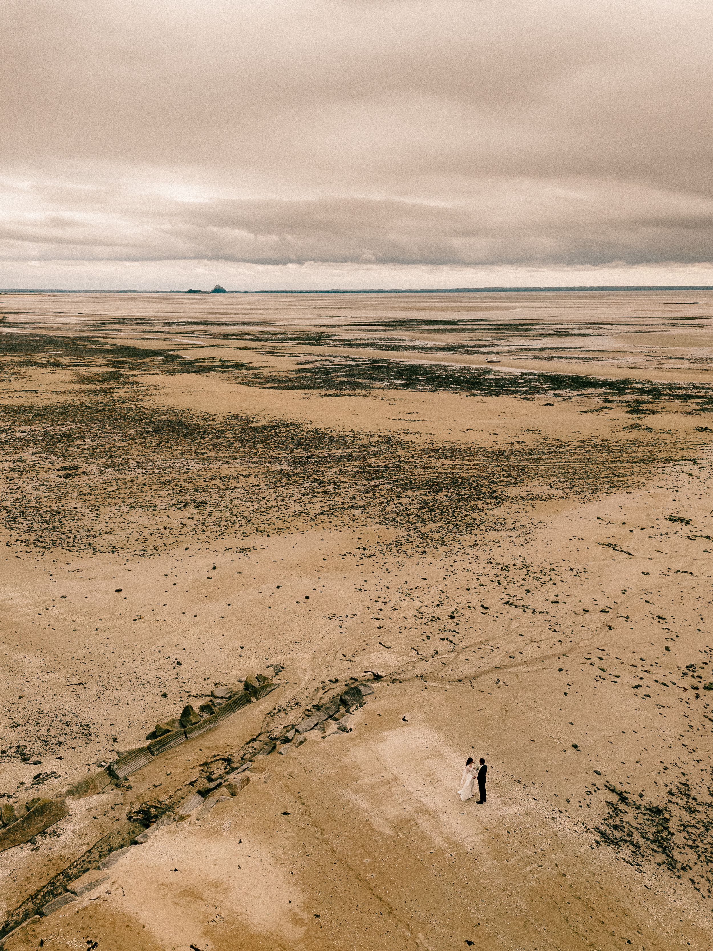 Aerial panoramic view of a vast desert landscape with distant mountains under moody clouds.