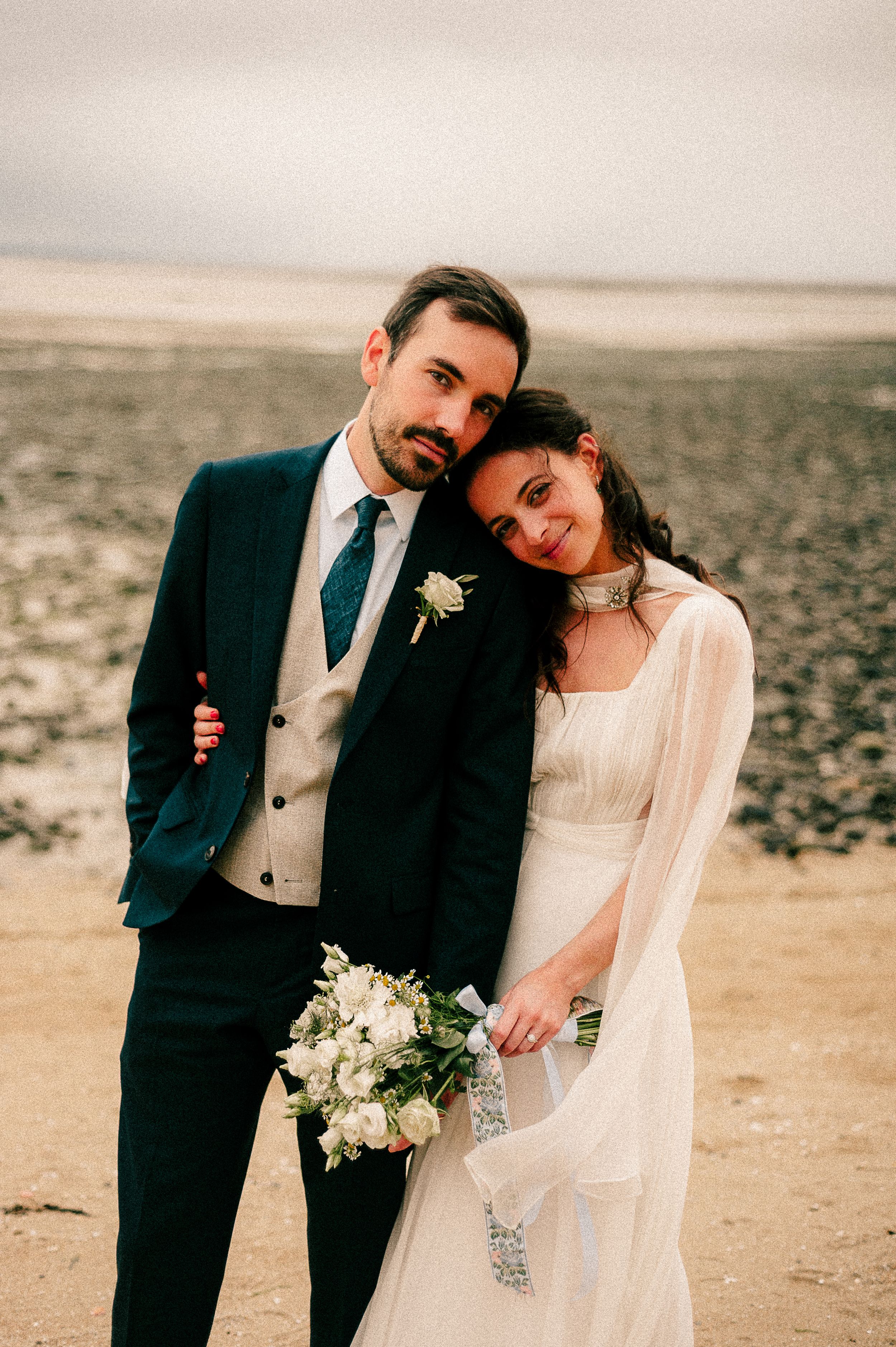 A romantic wedding portrait on a beach with the couple holding a white floral bouquet.