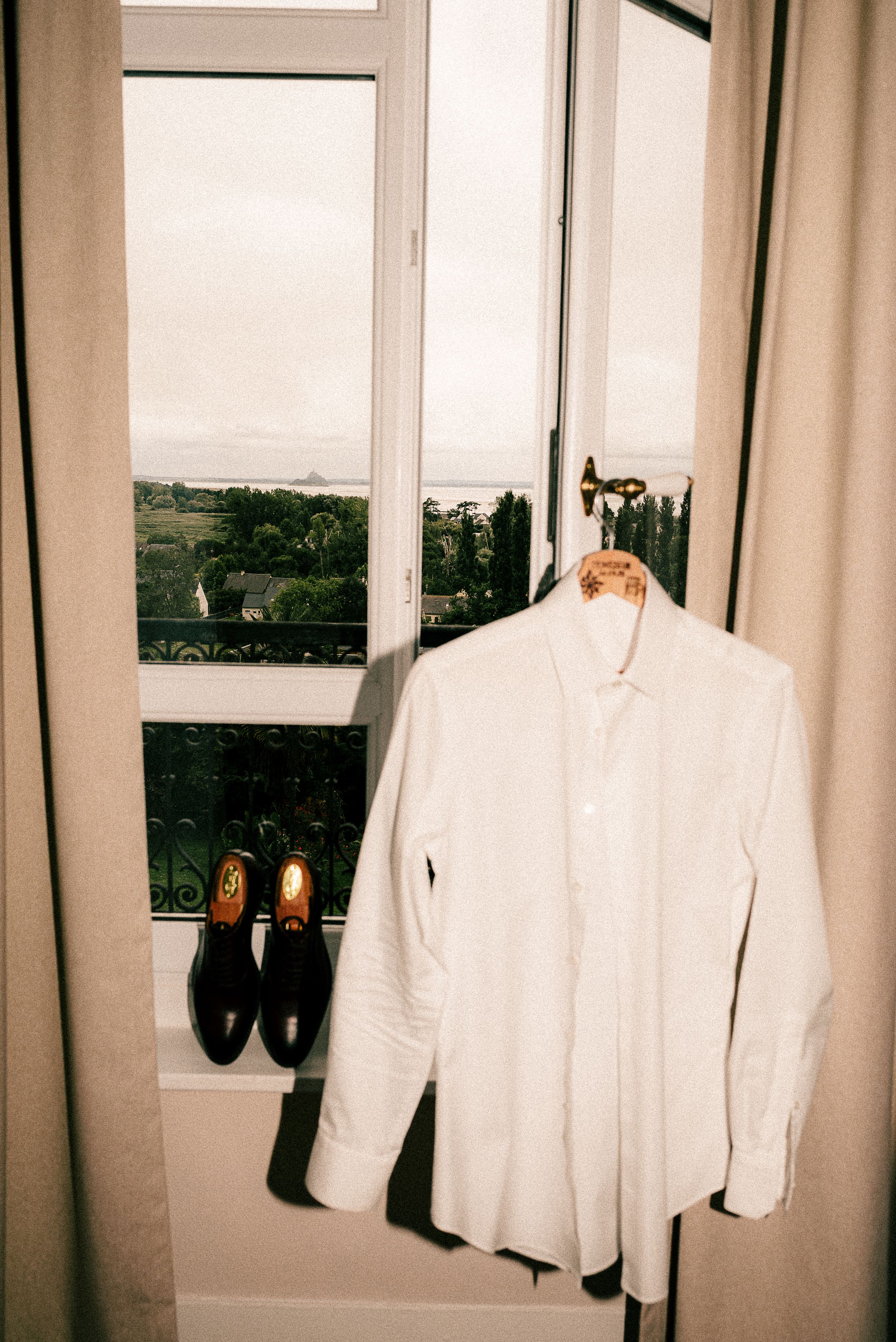 White formal jackets and dress shoes hanging by windows in a getting-ready room.
