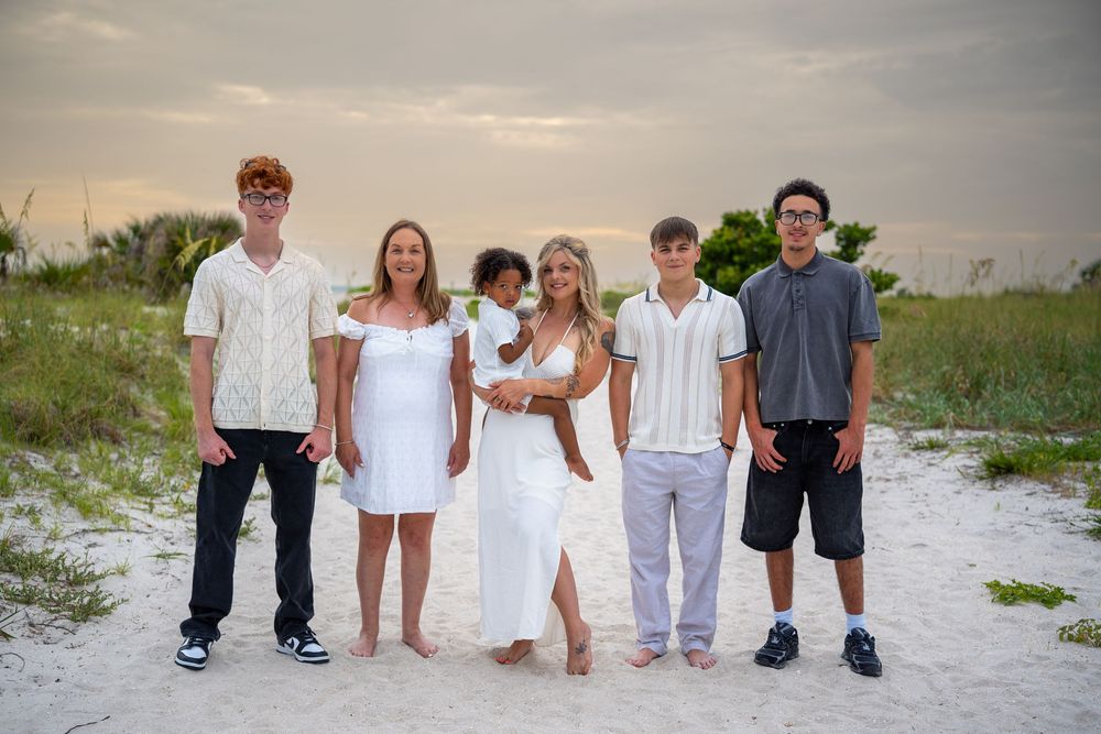 Family in white and neutral outfits posing together on sandy beach during sunset, lifestyle photography in Tampa Bay, Florida.