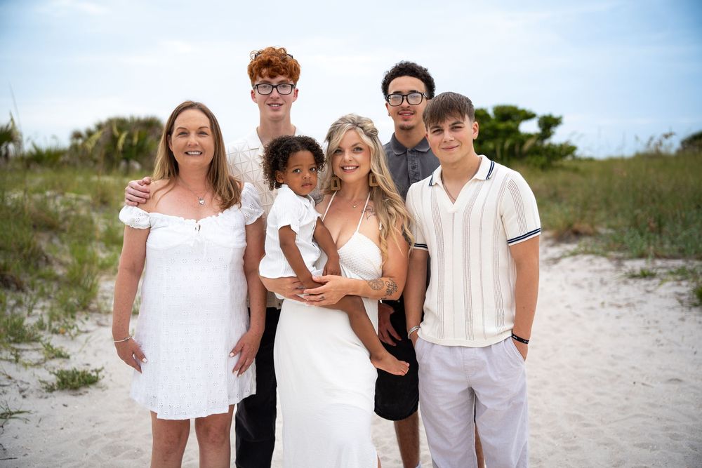 Family group portrait on sandy beach at sunset, wearing coordinated white and beige outfits — Tampa family beach photography.