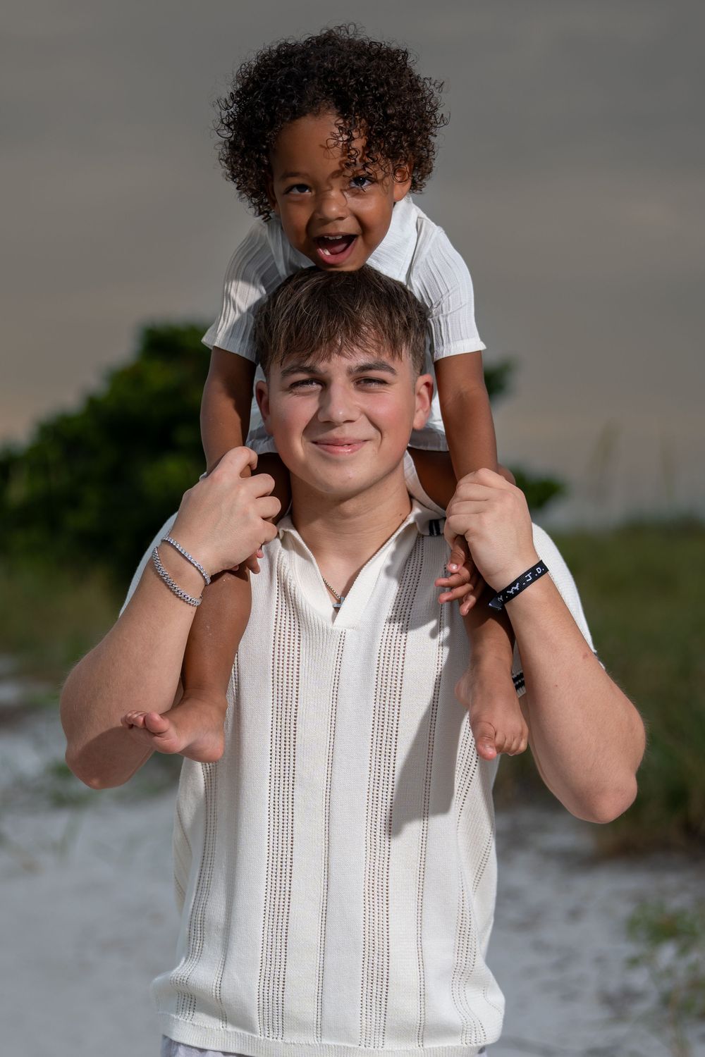 Playful parent holding child on shoulders outdoors in white clothing, candid family beach session in Tampa, Florida.