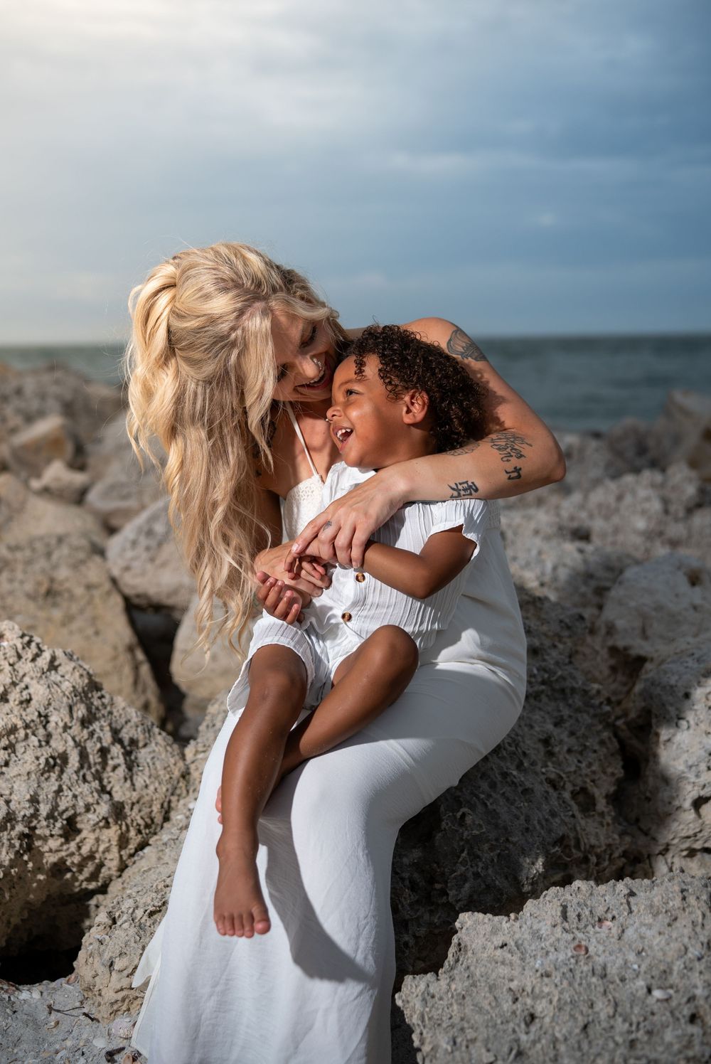 Couple in white outfits embracing on rocky coastal terrain at sunset, romantic beach photoshoot in Tampa Bay, Florida.