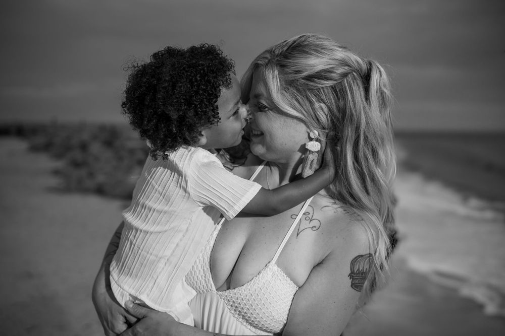 Black and white photo of mother hugging child on beach, emotional family photography in Tampa, Florida.