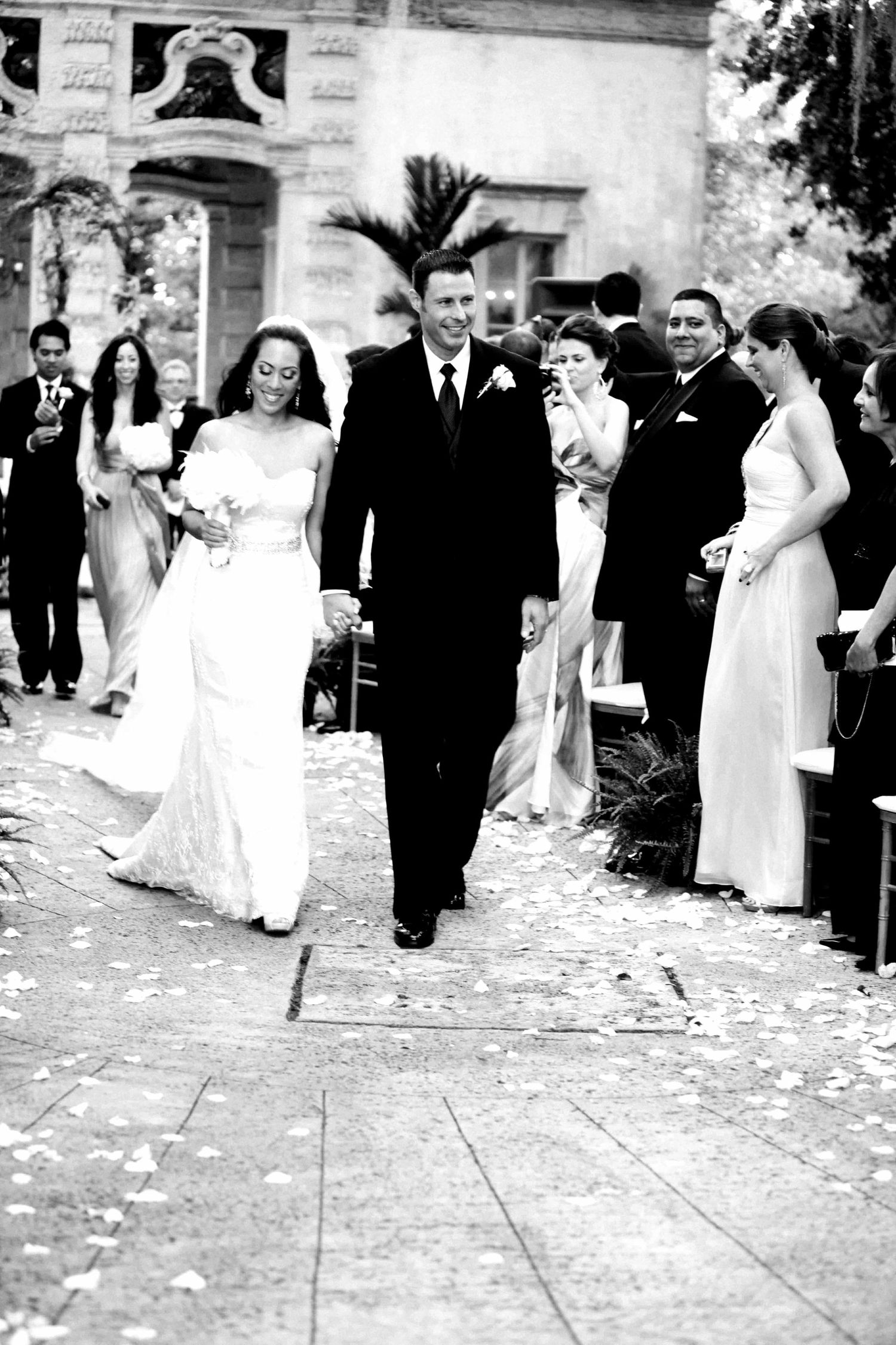A black and white sequence of wedding photos showing a couple walking together on a path covered with flower petals.