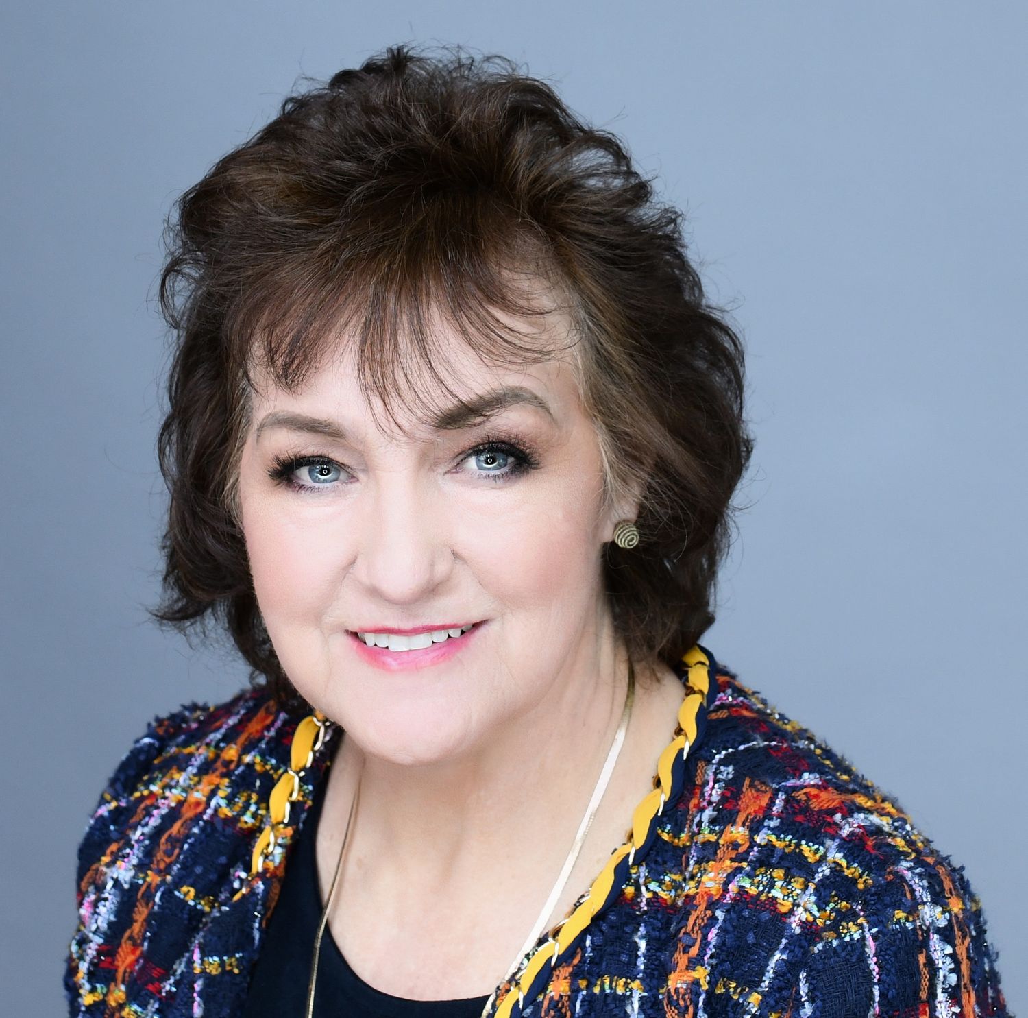 A professional studio portrait of a woman in a colorful patterned jacket with a warm smile.