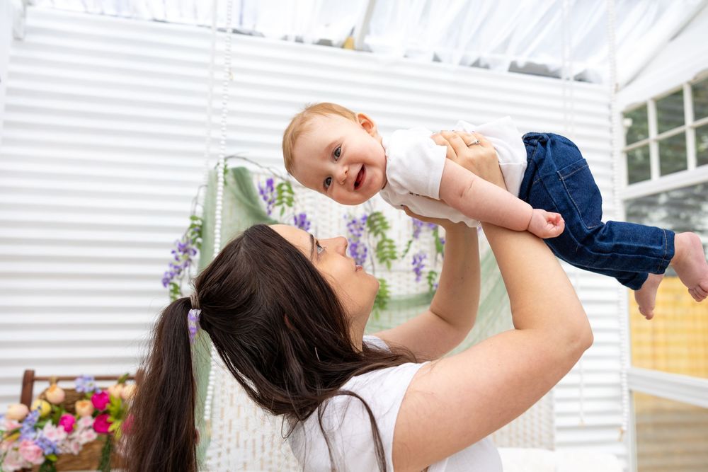 A joyful mother lifts her smiling baby in the air indoors, sharing a tender moment of love and happiness.