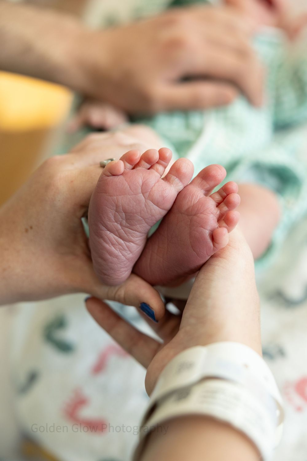Close-up of newborn baby feet held gently by adult hands in a hospital setting.