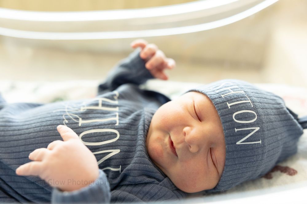 Newborn baby sleeping peacefully in a personalized blue ribbed outfit and matching hat.