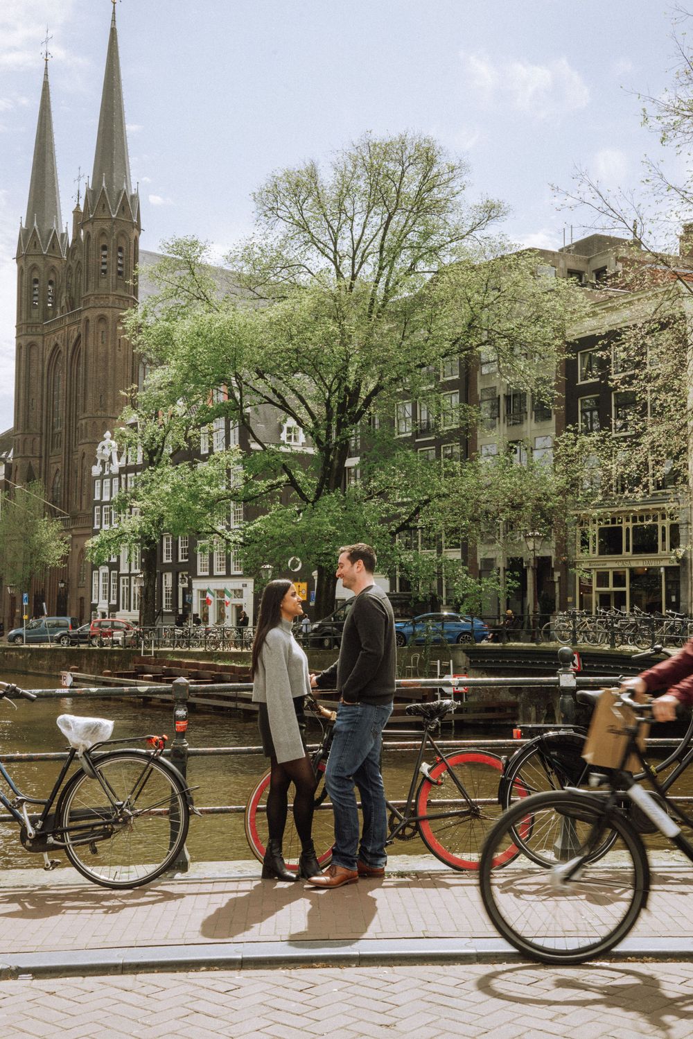 A scenic Amsterdam street with Gothic church spires, bicycles, and canal views.