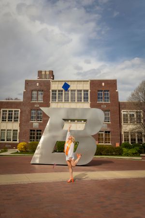 Boise state university graduate wearing white dress orange heels standing in front of the B