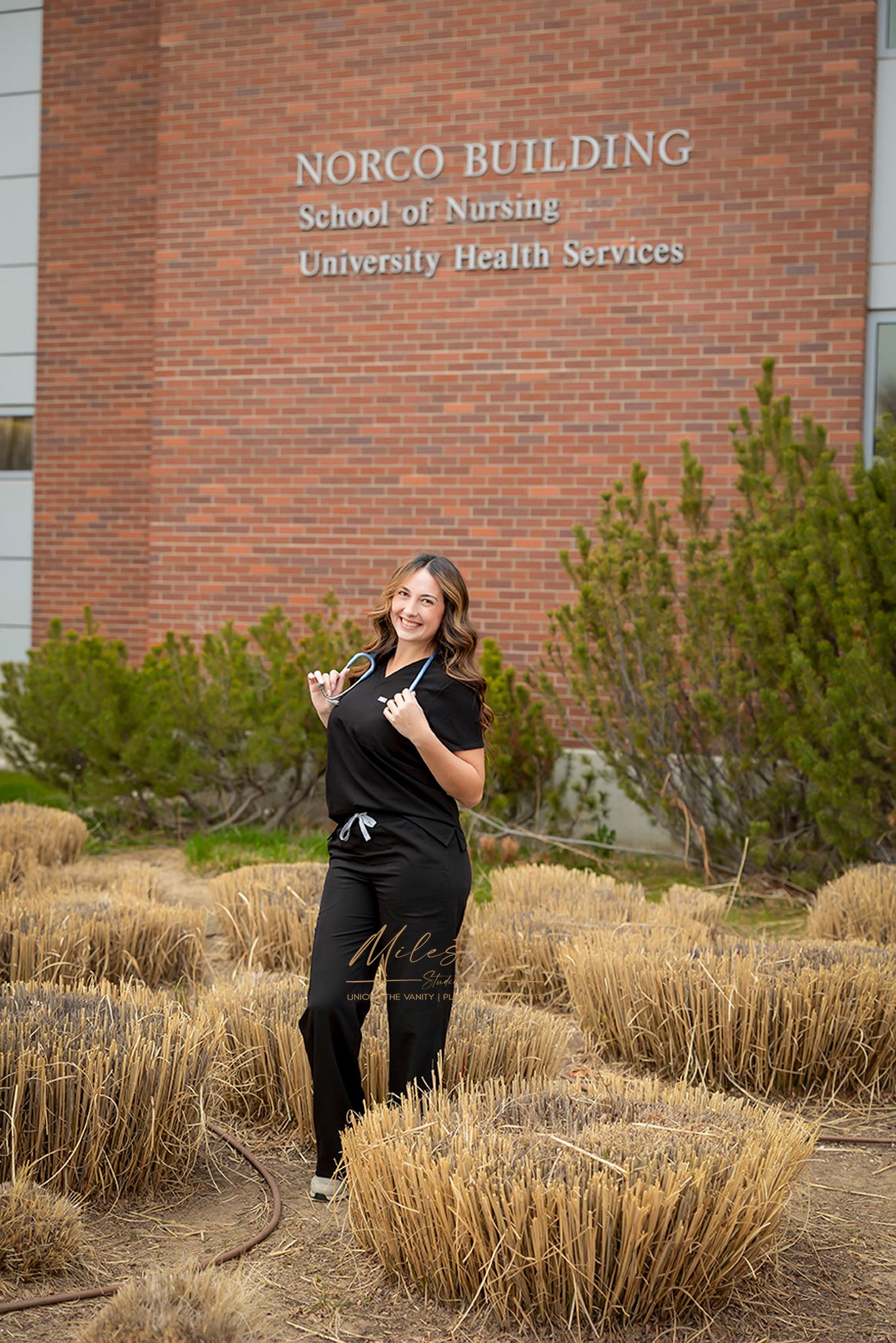 Boise State University graduate of nursing wearing  black scrubs by the Norco building