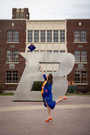 Boise State University graduate of nursing  wearing gown and throwing cap in front of the B