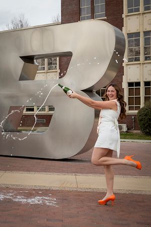 Boise State University graduate of nursing wearing white dress and popping champagne in front of the B