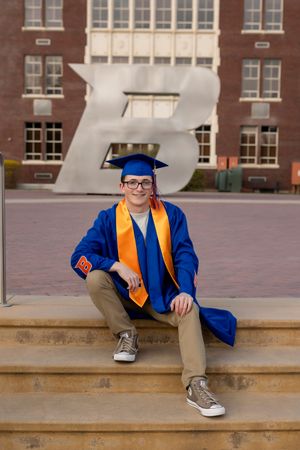 Male Boise State University graduate sitting on steps in front of the B wearing cap and gown