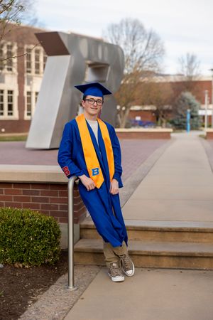 Male Boise State University graduate standing near the B wearing cap and gown