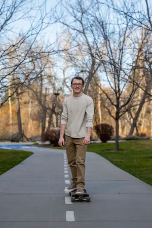 Male Boise State University graduate wearing street clothes on skateboard
