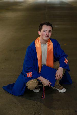 Male Boise State University graduate wearing street clothes in stairwell at Brady garage wearing gown in Brady garage