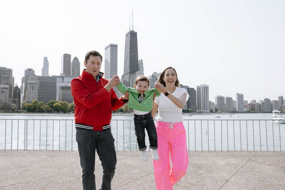 Family of three joyfully swinging child by Chicago skyline waterfront on a bright day.