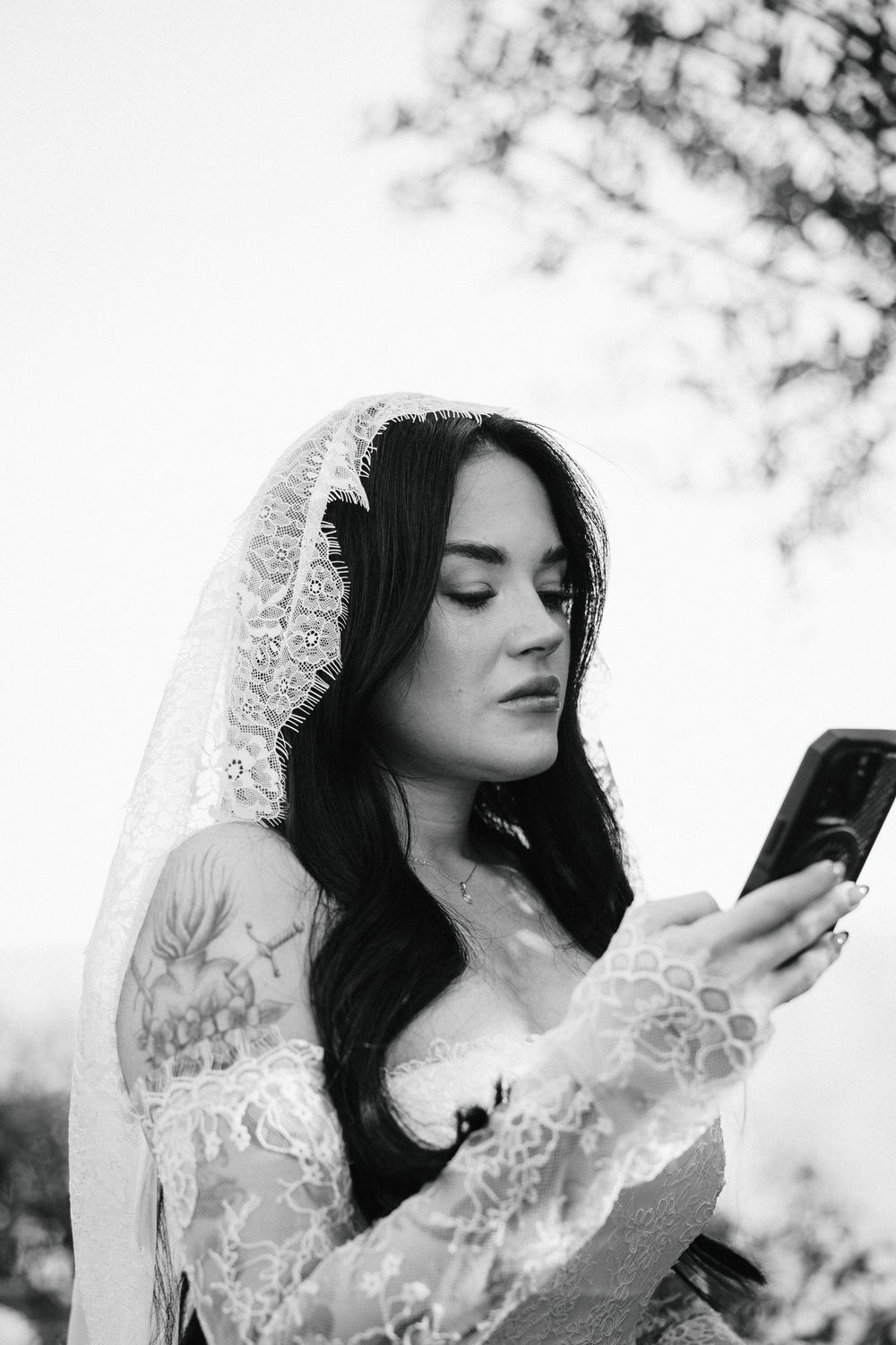Tattooed bride in lace wedding dress and veil reads her vows outdoors and gets emotional