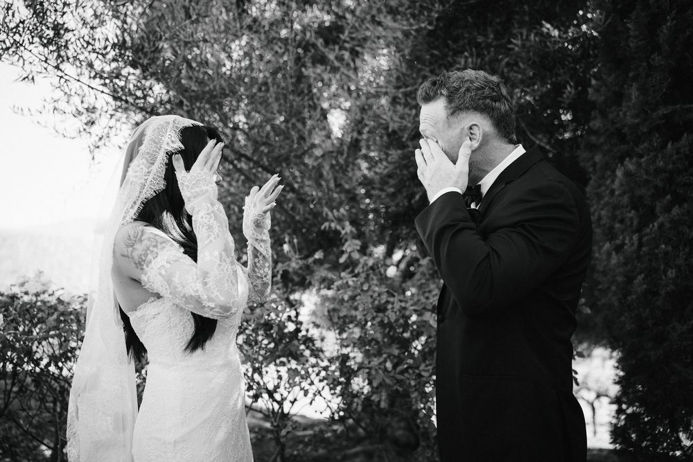 Emotional bride and groom crying during first look moment at outdoor wedding ceremony.