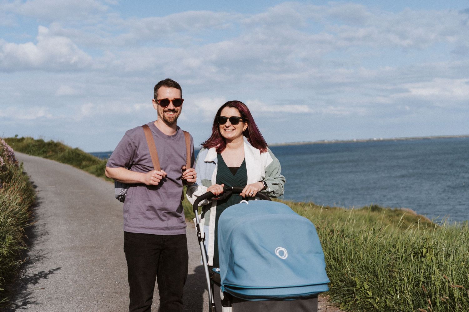 People riding bikes along a scenic coastal path with ocean views and green grass on a sunny day.