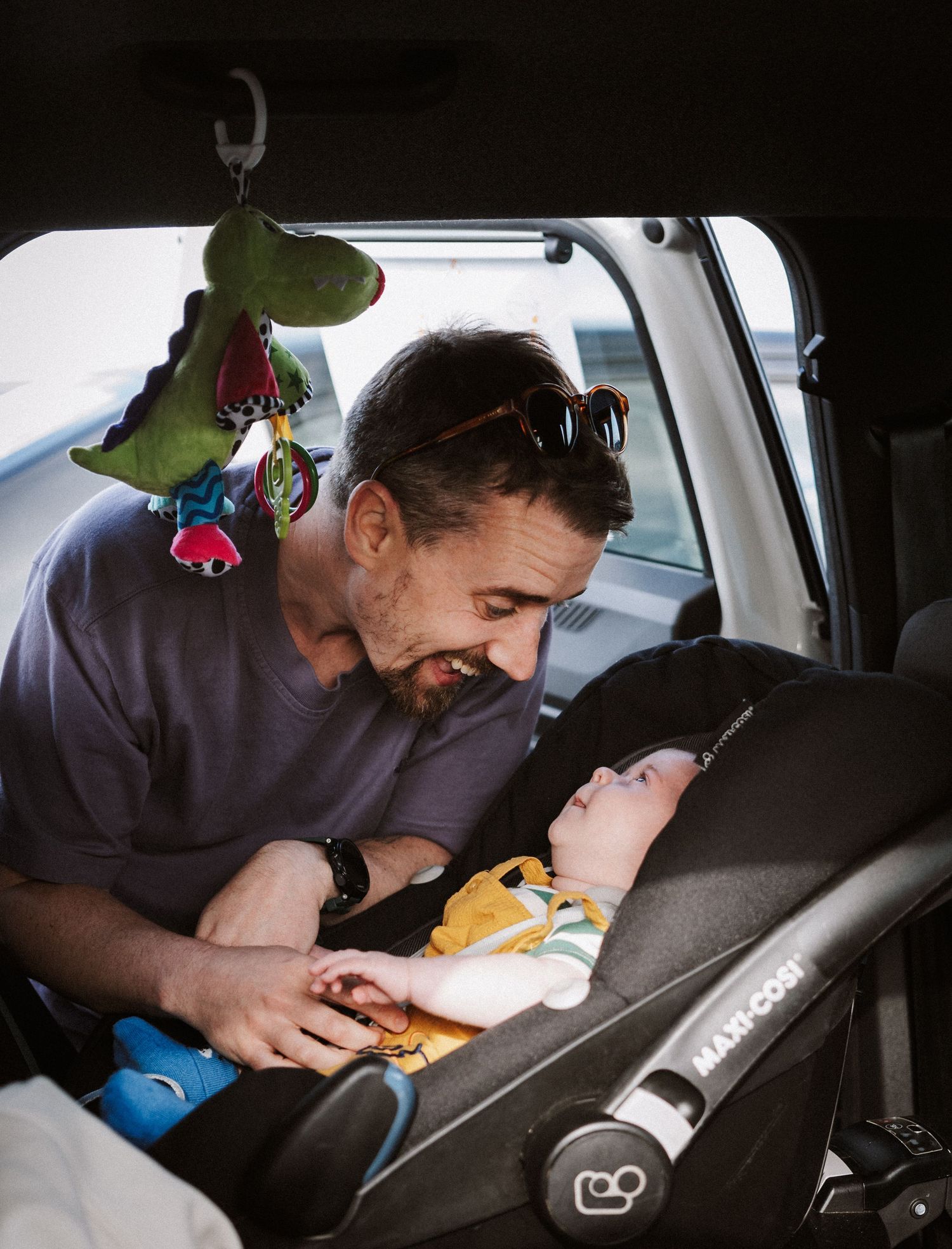 Parent leans over to check on sleeping baby in car seat during a car ride.