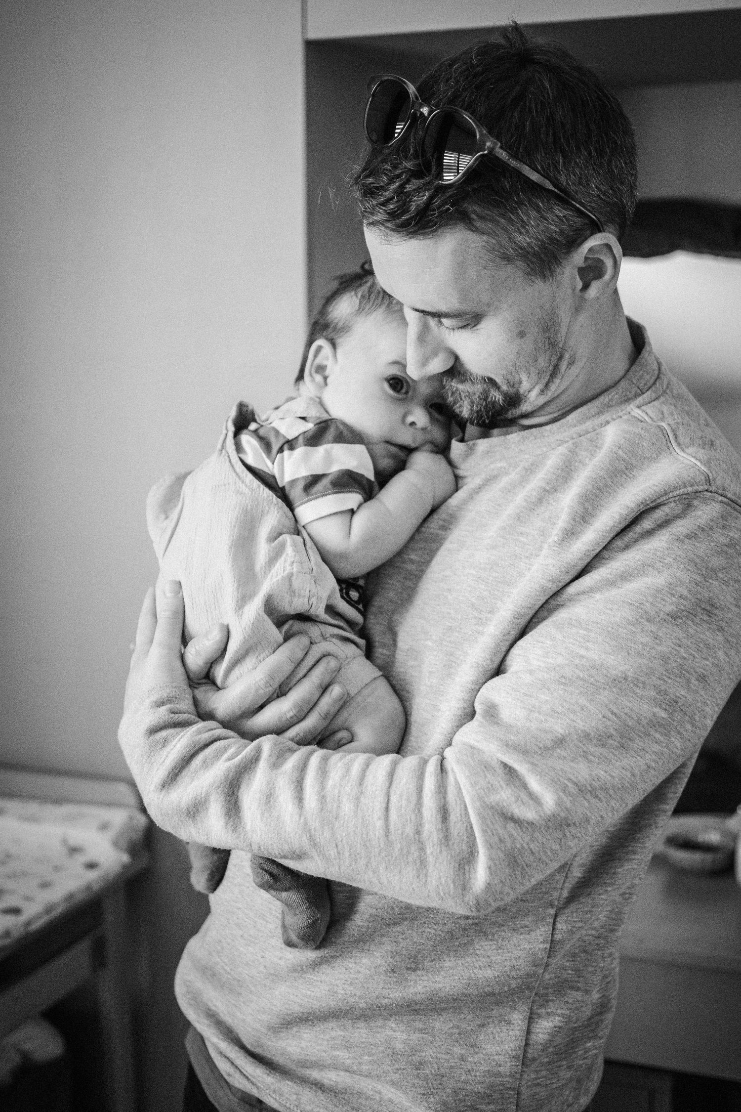 A series of black and white photos showing a tender moment between a parent and infant in a gray sweatshirt.