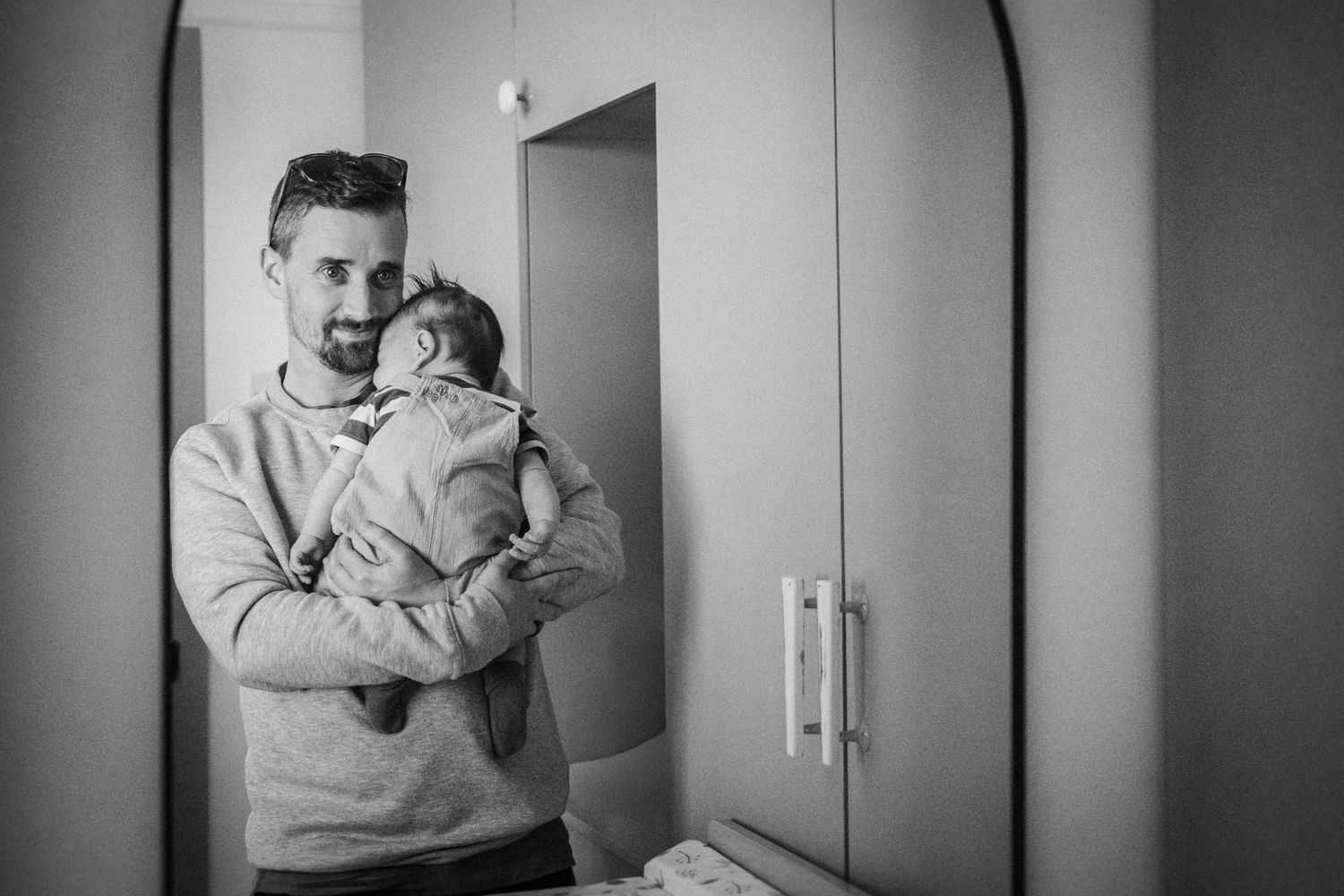 A tender black and white photograph showing a parent holding a small baby in a doorway.