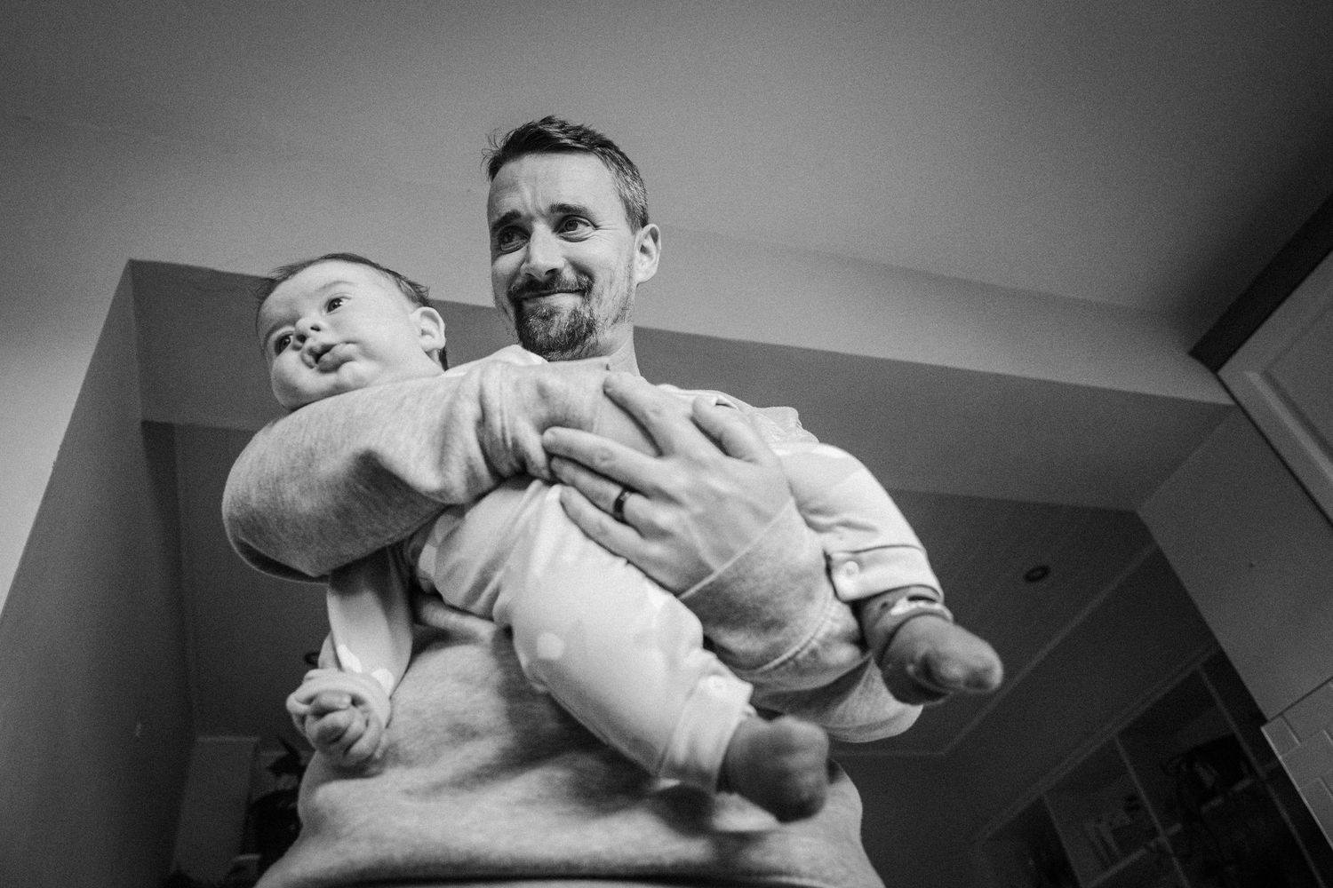 Black and white photograph showing a tender moment between a parent and baby in a cozy indoor setting.