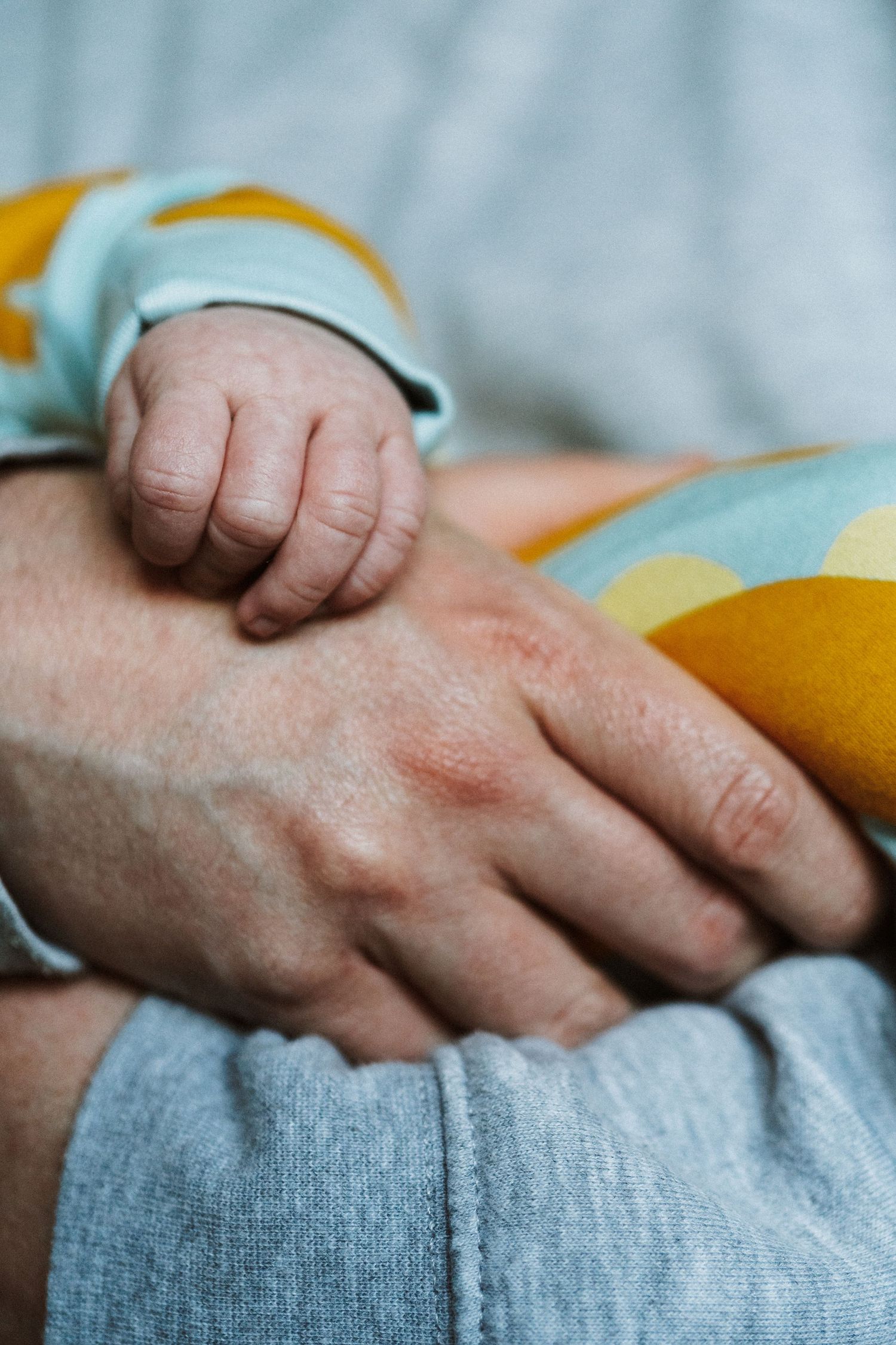 Close-up view of hands gently resting on soft blue and yellow fabric showing tender care and comfort.