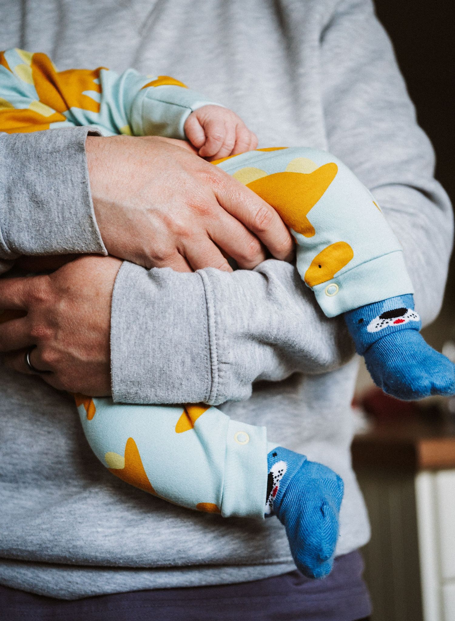 A close-up view of someone holding a baby wearing a gray sweatshirt and blue socks with yellow pattern sleepwear.